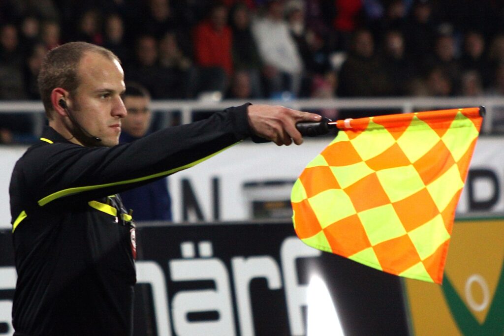 Árbitro assistente com bandeira levantada sinalizando posição de impedimento durante partida de futebol