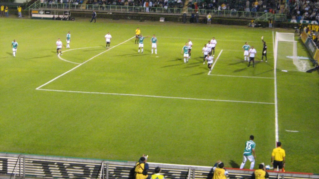 Jogadores posicionados em campo durante partida de futebol, ilustrando organização tática