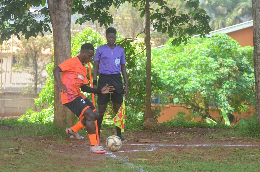 Jogador de uniforme laranja cobra escanteio ao lado da bandeirinha, observado pelo árbitro assistente.